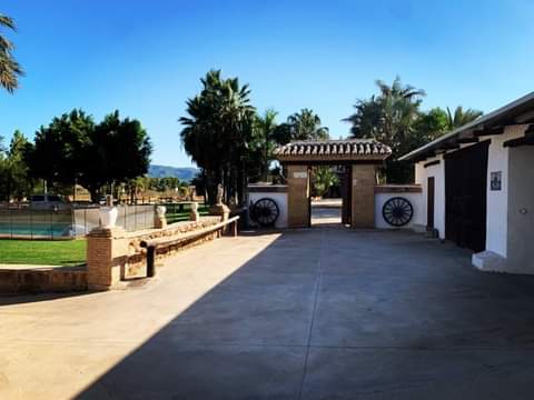 Image of entrance to main courtyard leading to events spaces at Cortijo La Rebanadilla.  Spanish traditional architecture and wheels adorn walls either side of entrance.